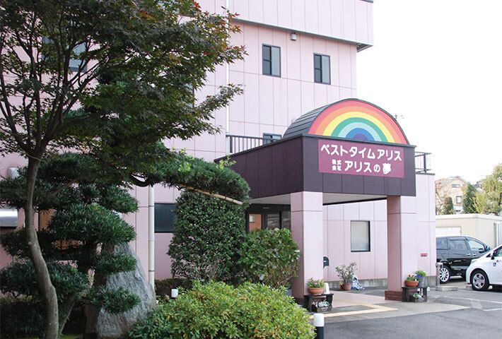敷地内にはたくさんの木が植えられ、建物の玄関には車寄せが付いている。駐車場があり、車が止まっている。