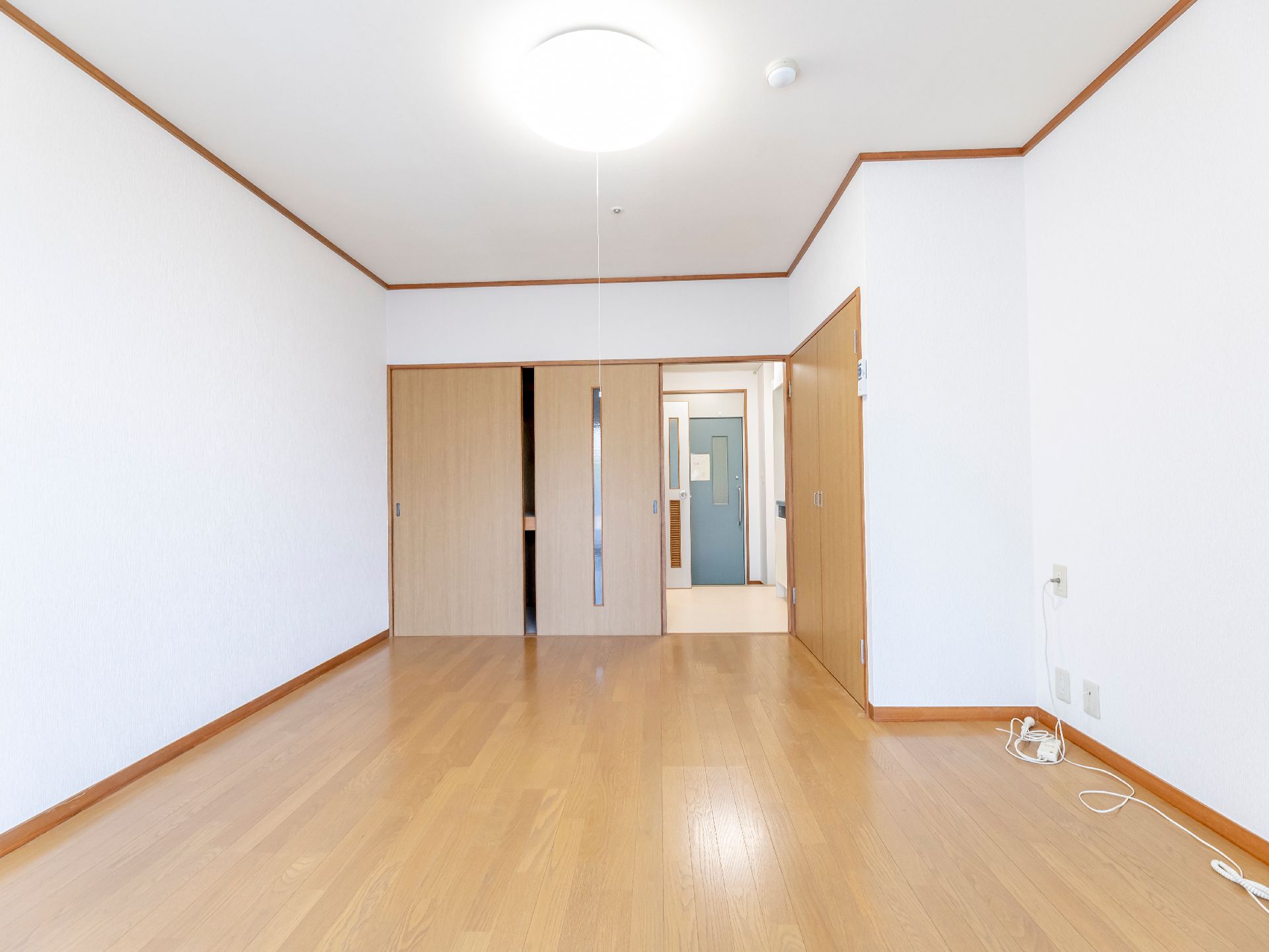 白い壁とフローリングの床に囲まれた何も置かれていない部屋