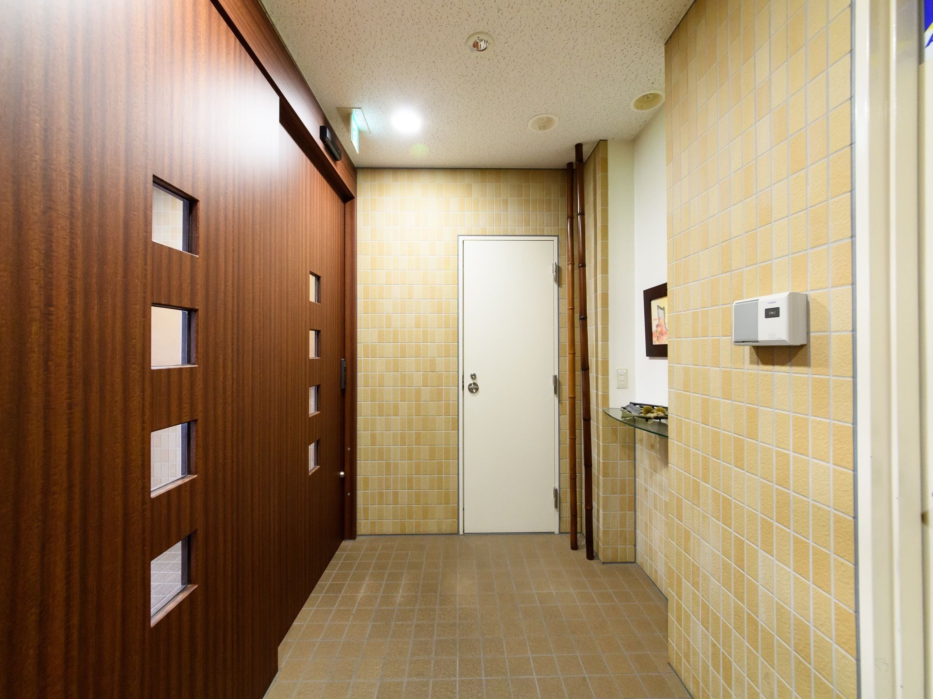 玄関ホールには茶色く大きなスライド式の扉が設置されている。近くには白い扉、竹のようなものが2本置かれている。