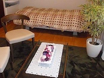 ベッドと背の低いテーブル、いす、観葉植物が置いてある施設内の居室の様子