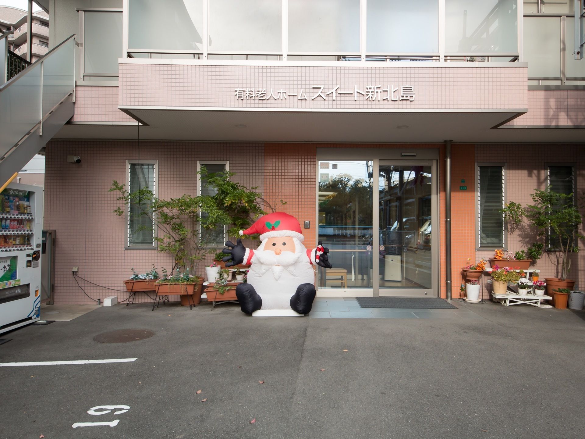 ピンクのタイル張りの壁が特徴的な外観をしており、エントランスのすぐそばに観葉植物やサンタの置物が飾られている。