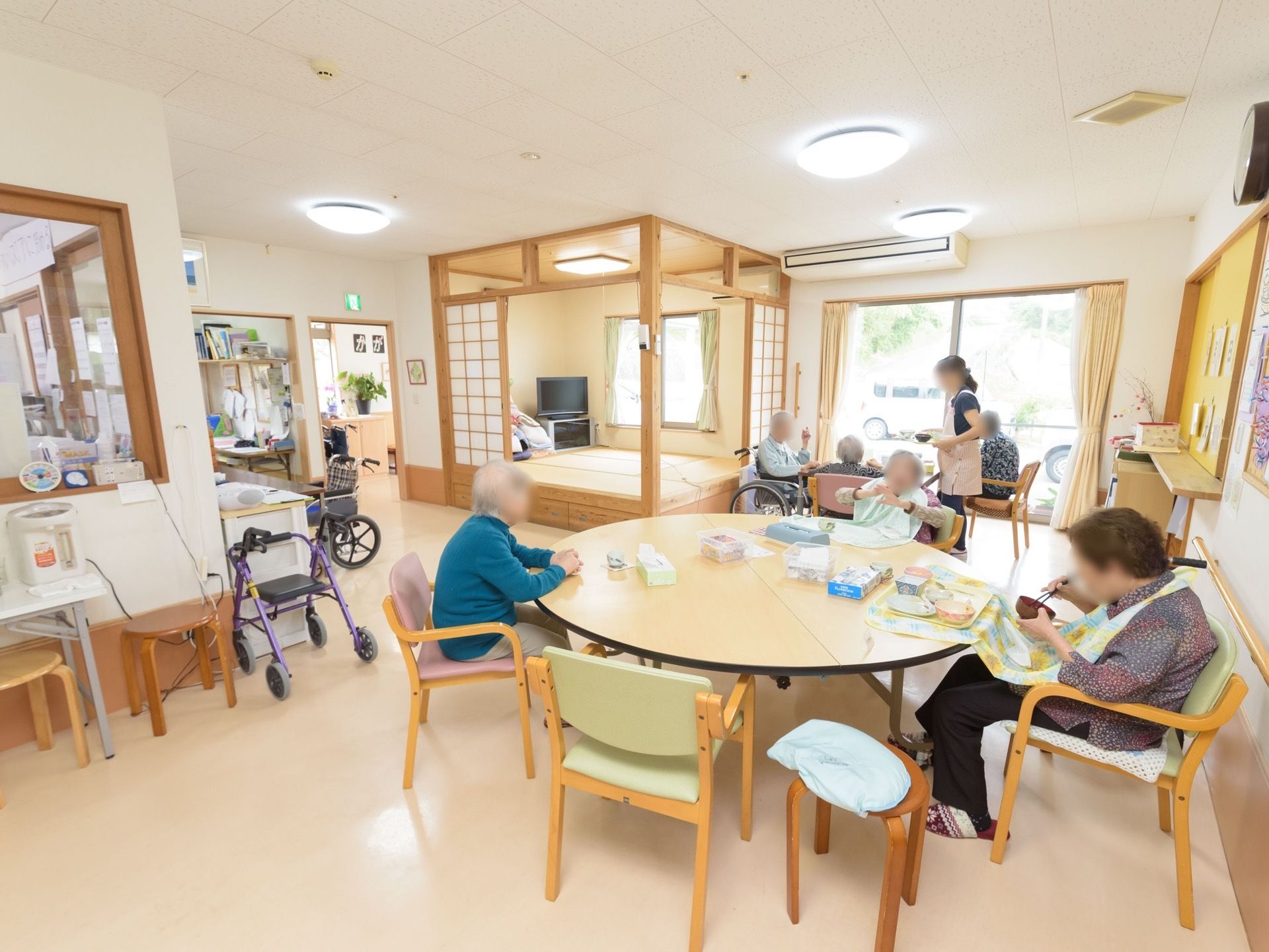 丸いテーブルを囲むように、入居者様が座って食事をしている様子である。奥には障子で囲まれた、畳のスペースがある。