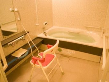一般の家庭と同じようなサイズの浴槽が置かれた白い浴室にはシャワーと手すり、シャワーチェアも設置されている。