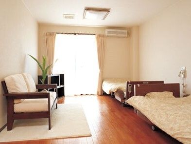 フローリングの居室。カーテン付きの窓とエアコン、ベッドが２つあり、観葉植物やテレビ、ソファもついている。