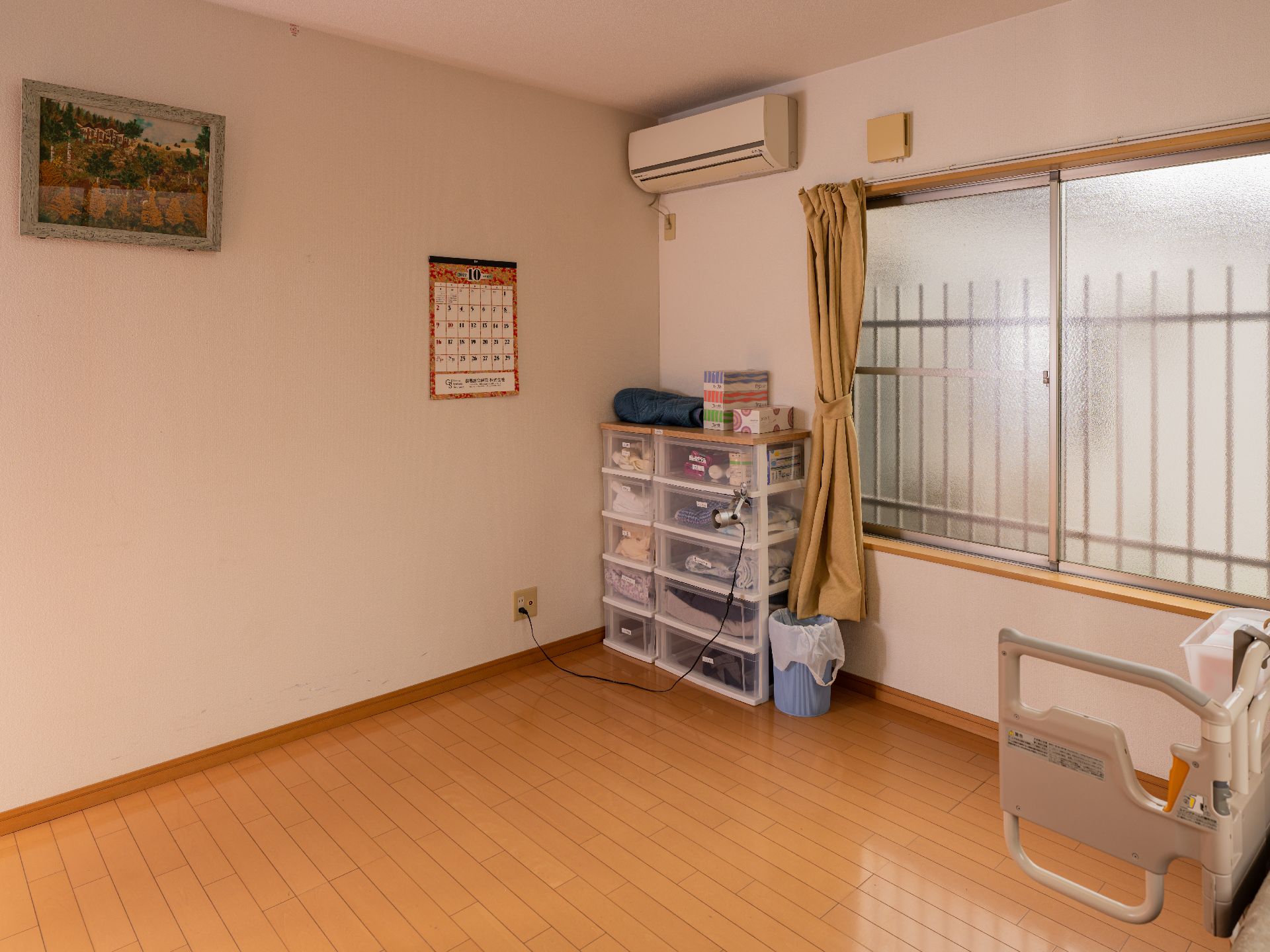 屋外で笑顔で過ごしている車いすの高齢男性と付き添いの若い女性スタッフ。後ろには民家もある。