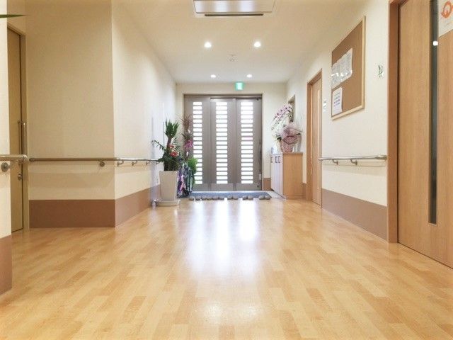 手すりが両サイドにある廊下の突き当りにある玄関。段差がなくスリッパが並べられ、観葉植物や花も飾られている。