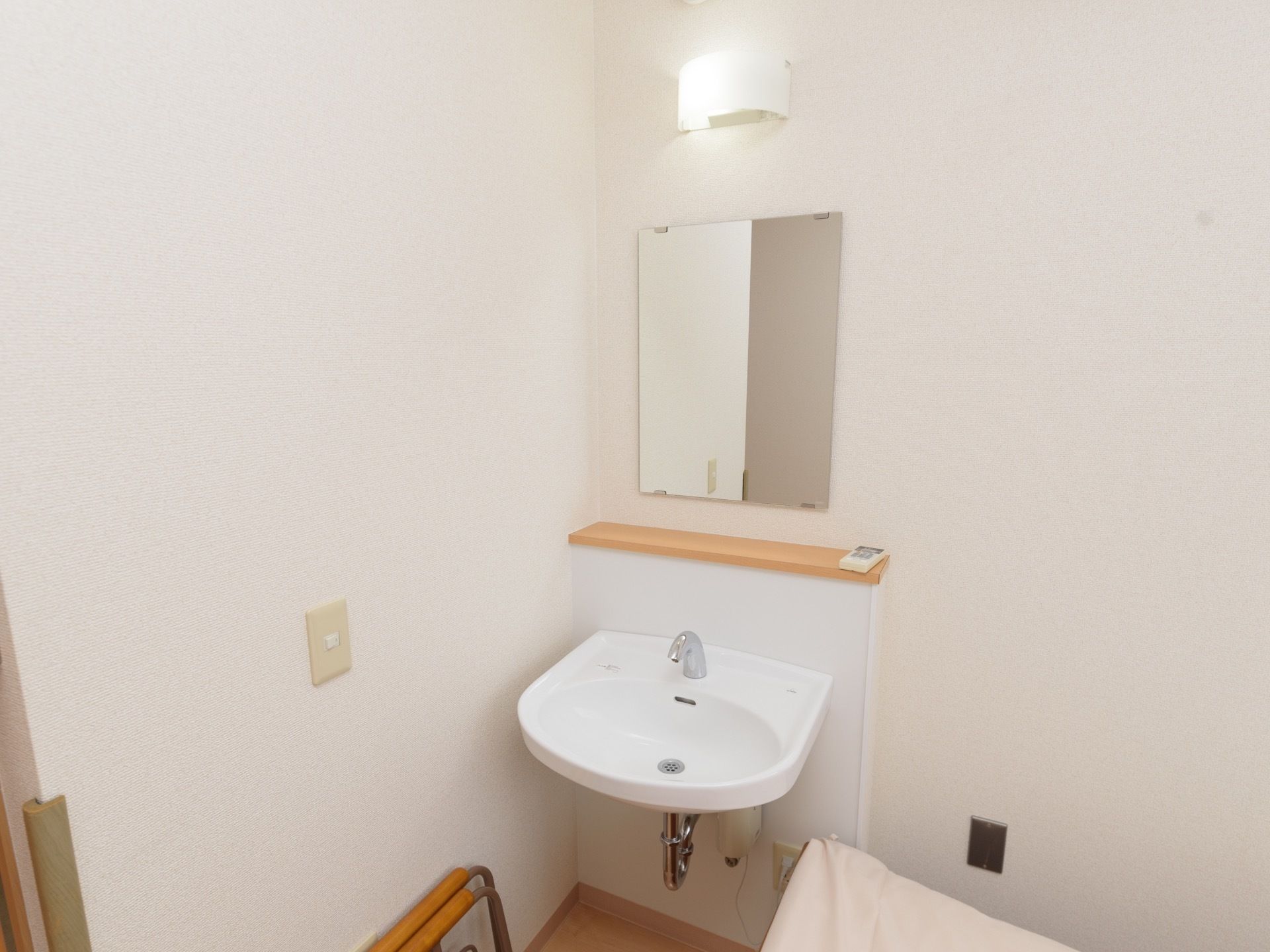 居室に白を基調としたフットレスタイプのシンプルな洗面台がある。壁には、照明や鏡が取り付けられている。