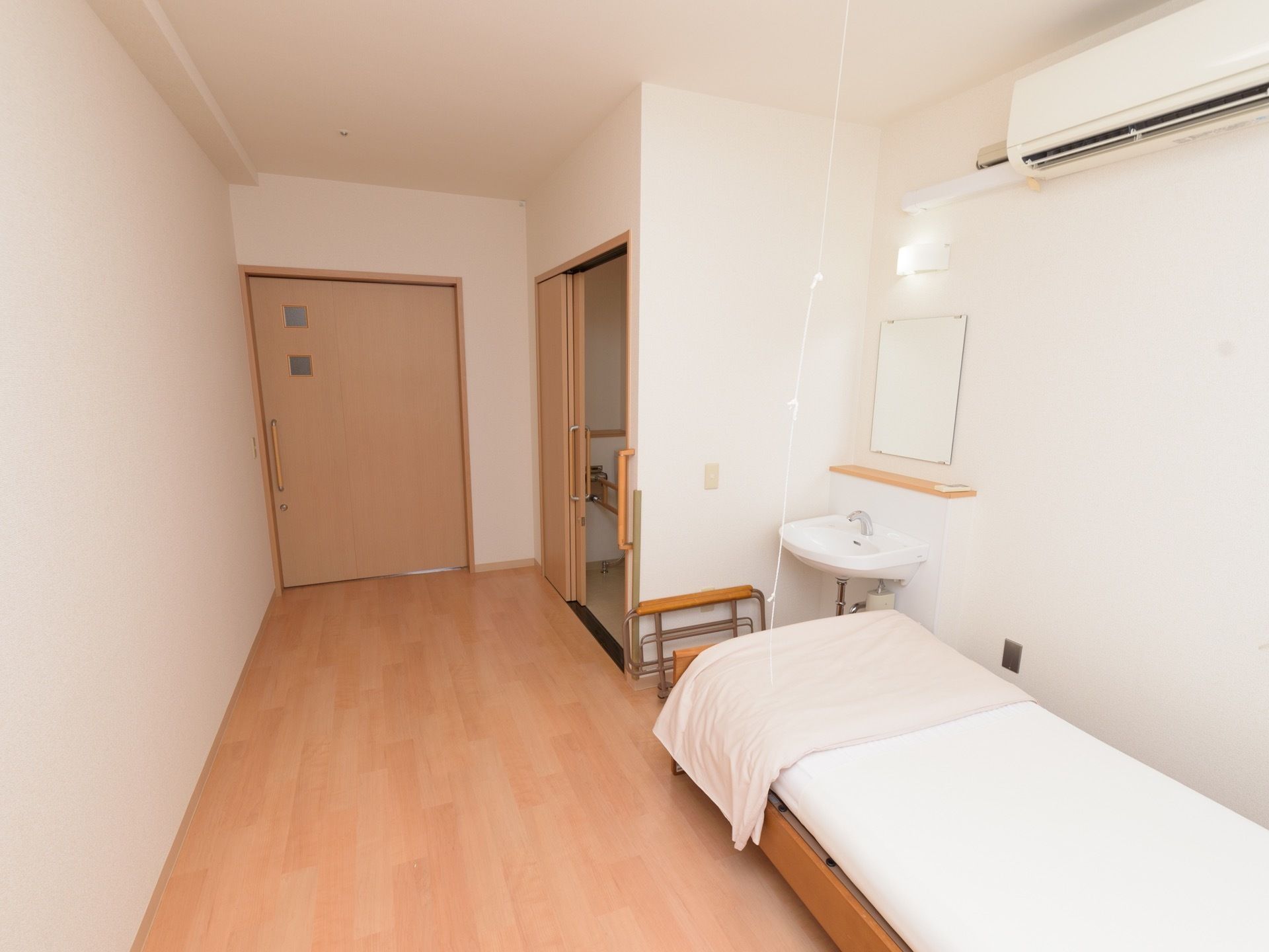 洗面台やトイレが備え付けられている居室で、床は木目調のフローリングとなっている。壁にはエアコンが設置されている。