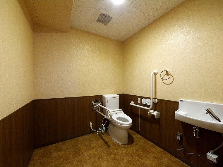 広いトイレにはエル字型の手すりと可動式の手すり、呼び出しボタンや手洗い場が設置されている。