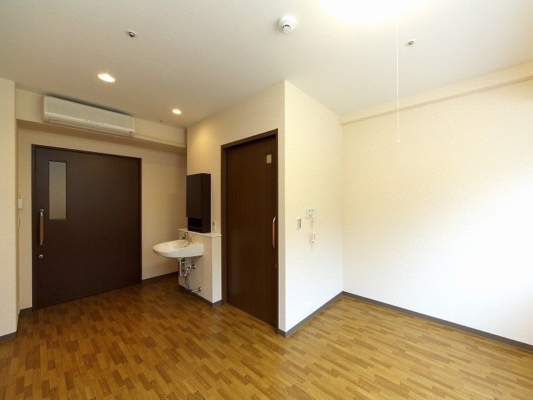白い壁にフローリングのフロア。居室ドアやトイレのドアはダークブラウンで、エアコンや洗面所も付いている。