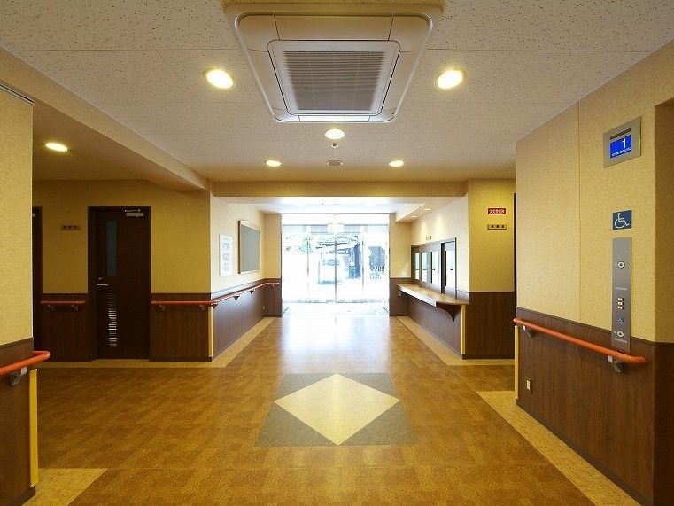 玄関には大きな自動ドアが付き、受付にはカウンターがある。手すりはオレンジでよく目立つ。