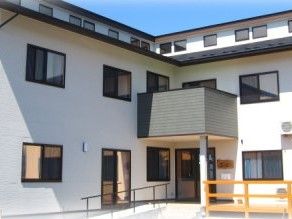 2階建ての建物の外観写真。雨除けのひさしとスロープ付きの玄関