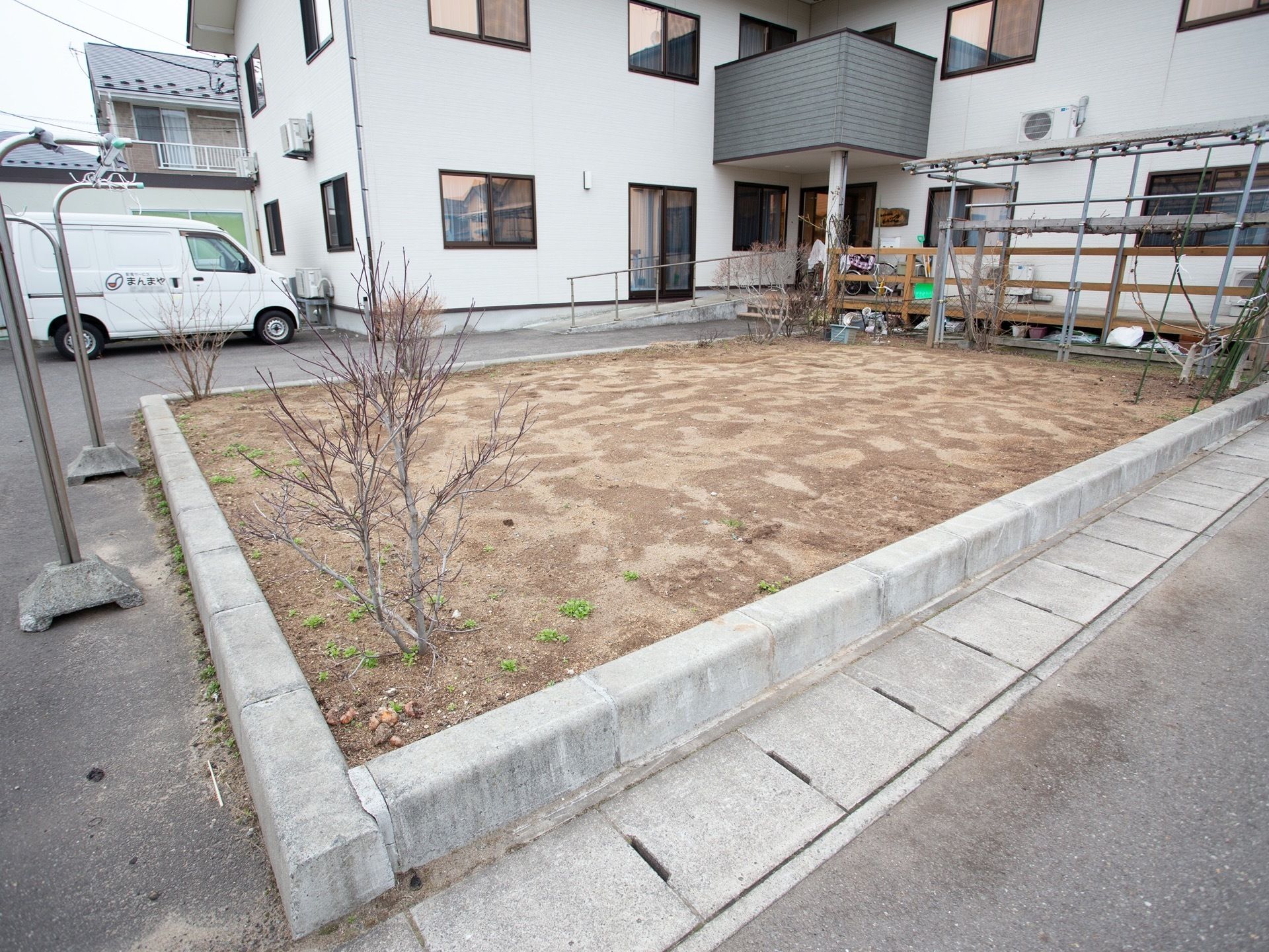 施設の敷地内には、建物の前にコンクリートブロックで囲った土地がある。茶色の土がむき出しになり、四方の角に木が植えられている。