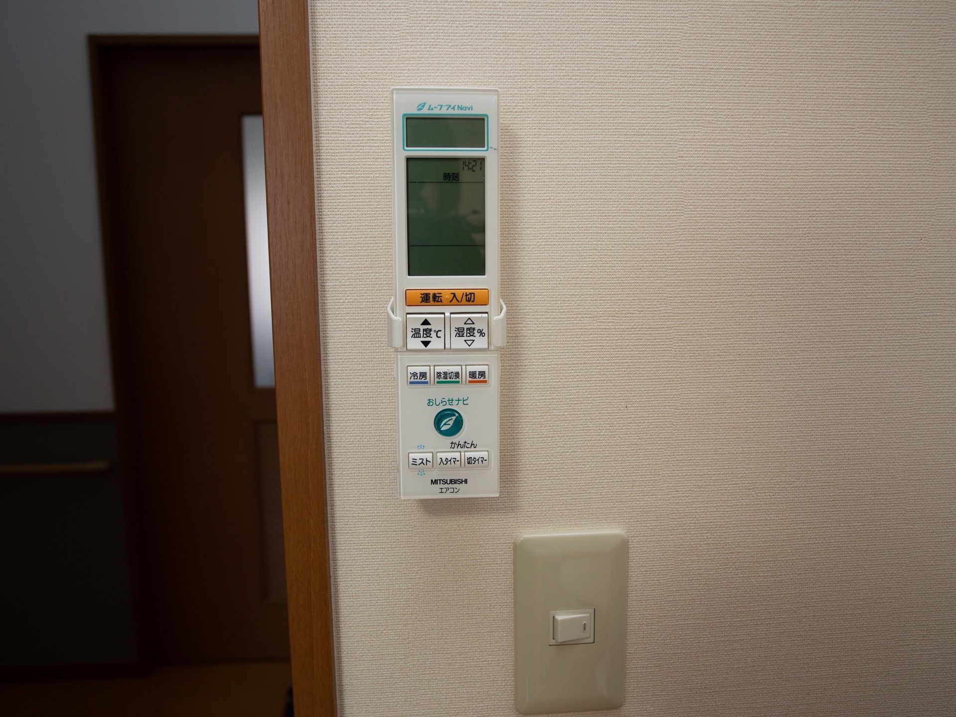 白色の居室の壁に取り付けられたストッパーに、エアコンのリモコンがはめられている。液晶画面が大きく、冷暖房の切り替えができるようになっている。