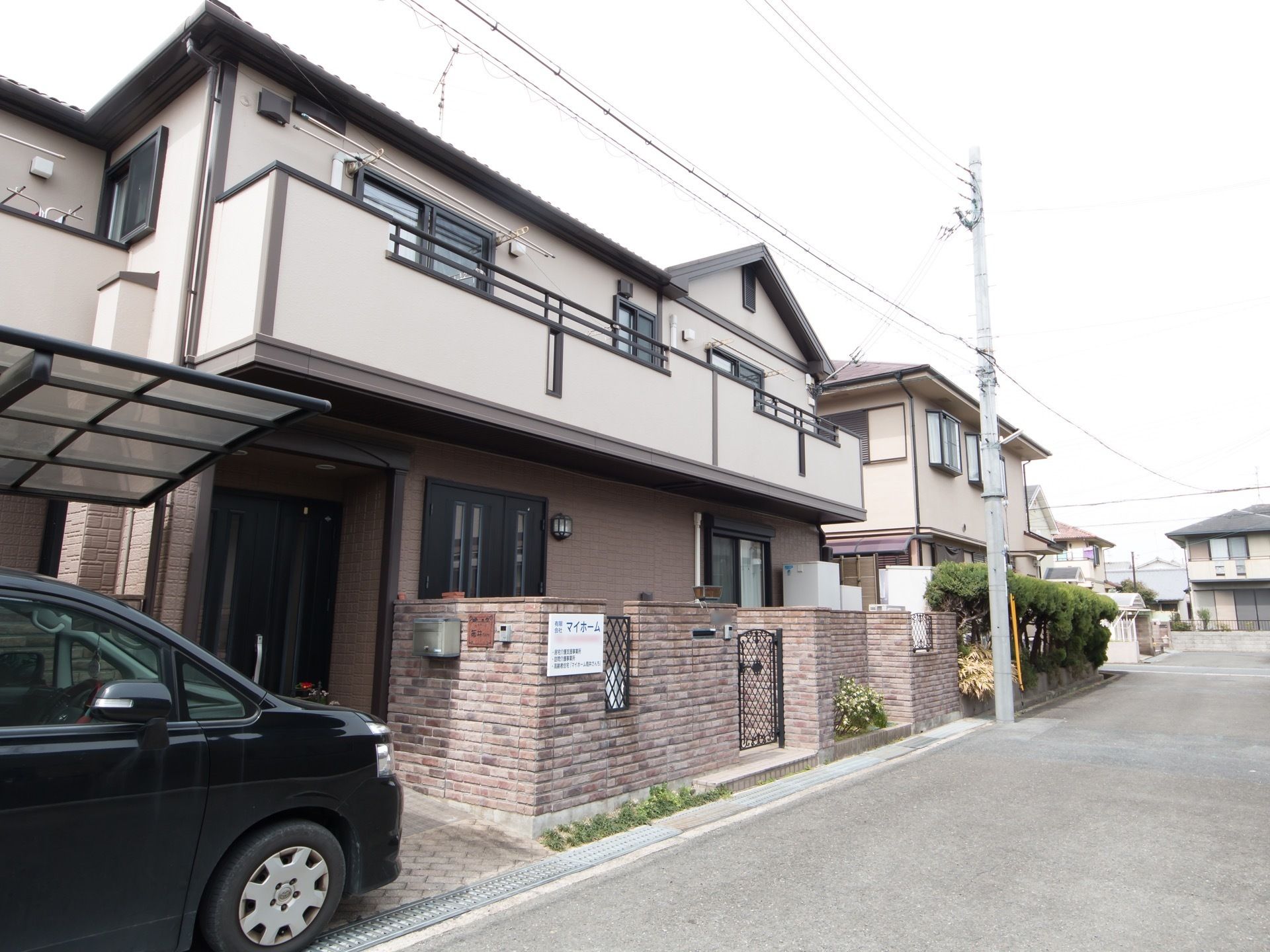 落ち着いた色に施された２階建の一軒家風建物である。カーポートには車が1台停まっている。外壁には施設名が記された看板が設置されている。