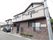 落ち着いた色合いに施された一軒家風の建物である。駐車スペースが設けられており、車が1台停まっている。