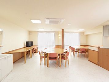 六角形のダイニングテーブルが複数置かれた食堂。左の壁際には長方形のテーブルがあり、テレビも置かれている。