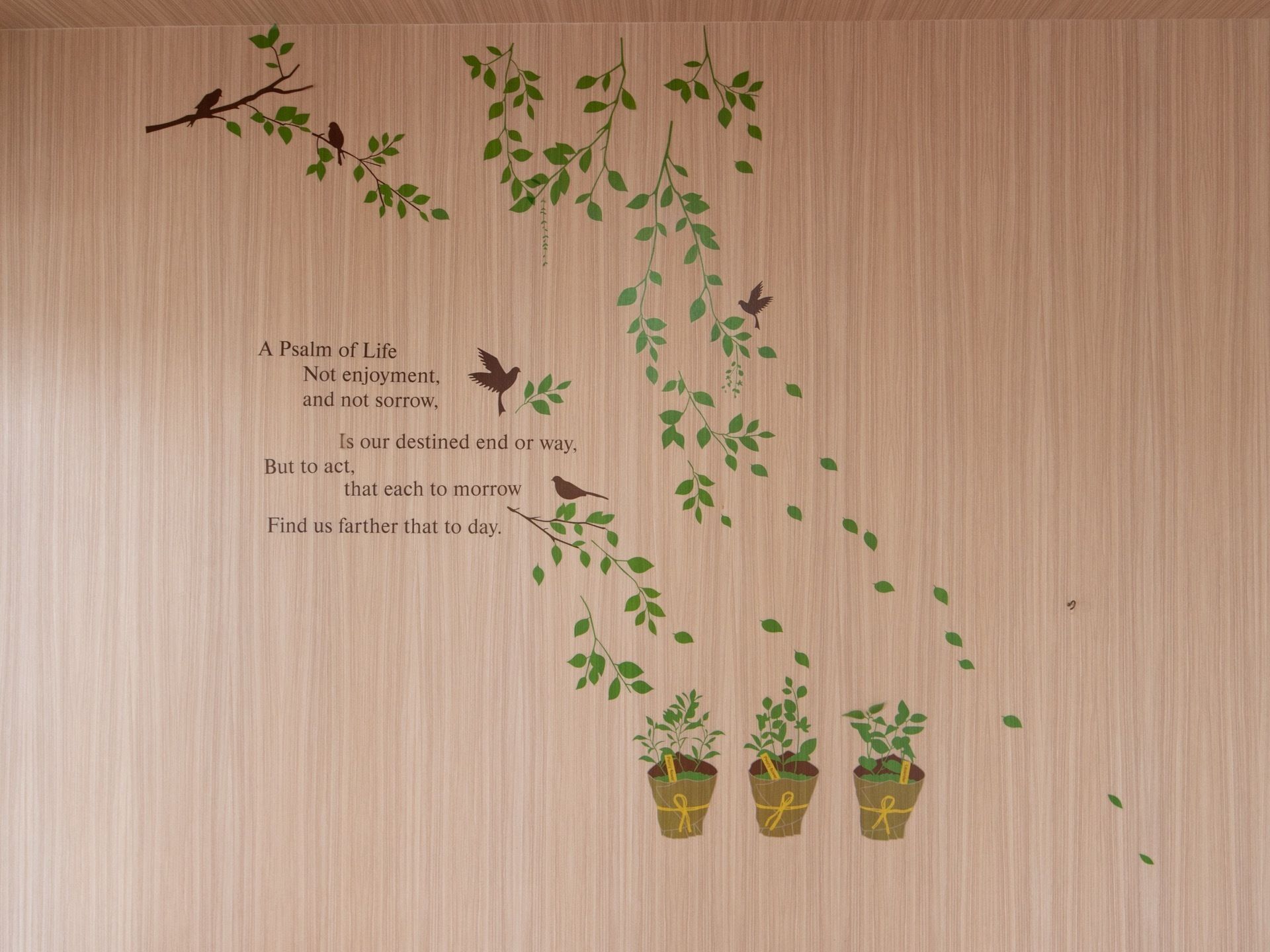 居室にある木目の壁面に、緑の葉の生い茂った木の枝や鉢植え、小鳥などの絵と、英語の文章が書かれている。