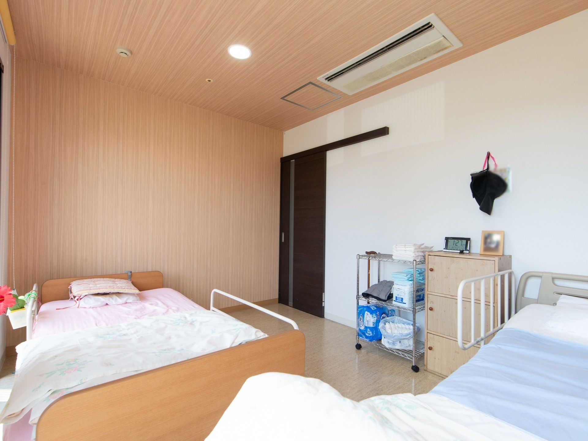 すっきりとした近代的なデザインの居室。室内に２台の介護用ベッドや収納棚が置かれていて、天井には空調設備が備え付けられている。