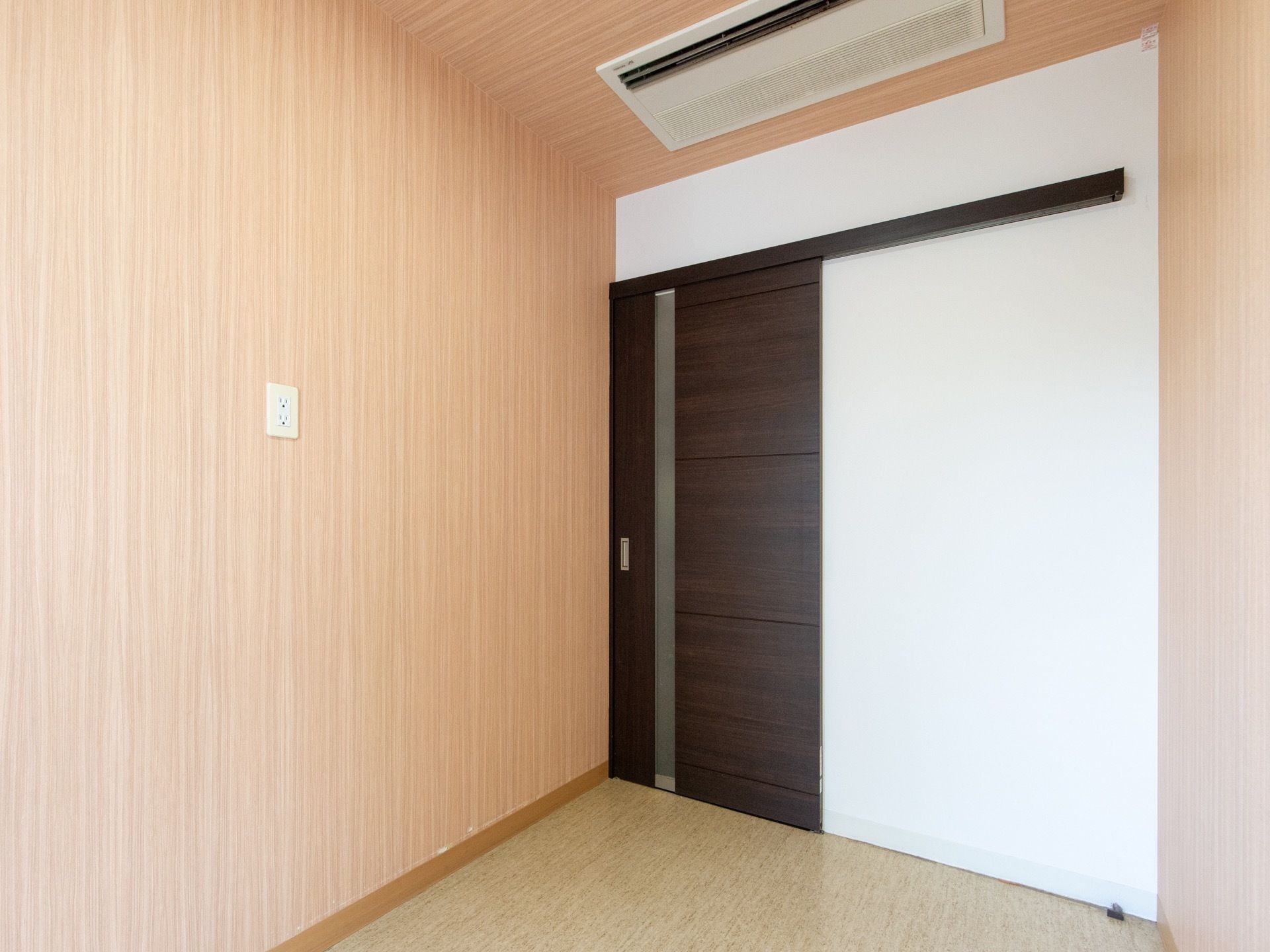 濃い茶色の木目模様で、引き戸になっている居室の扉。上の天井には、埋込み式の空調設備が備え付けられている。