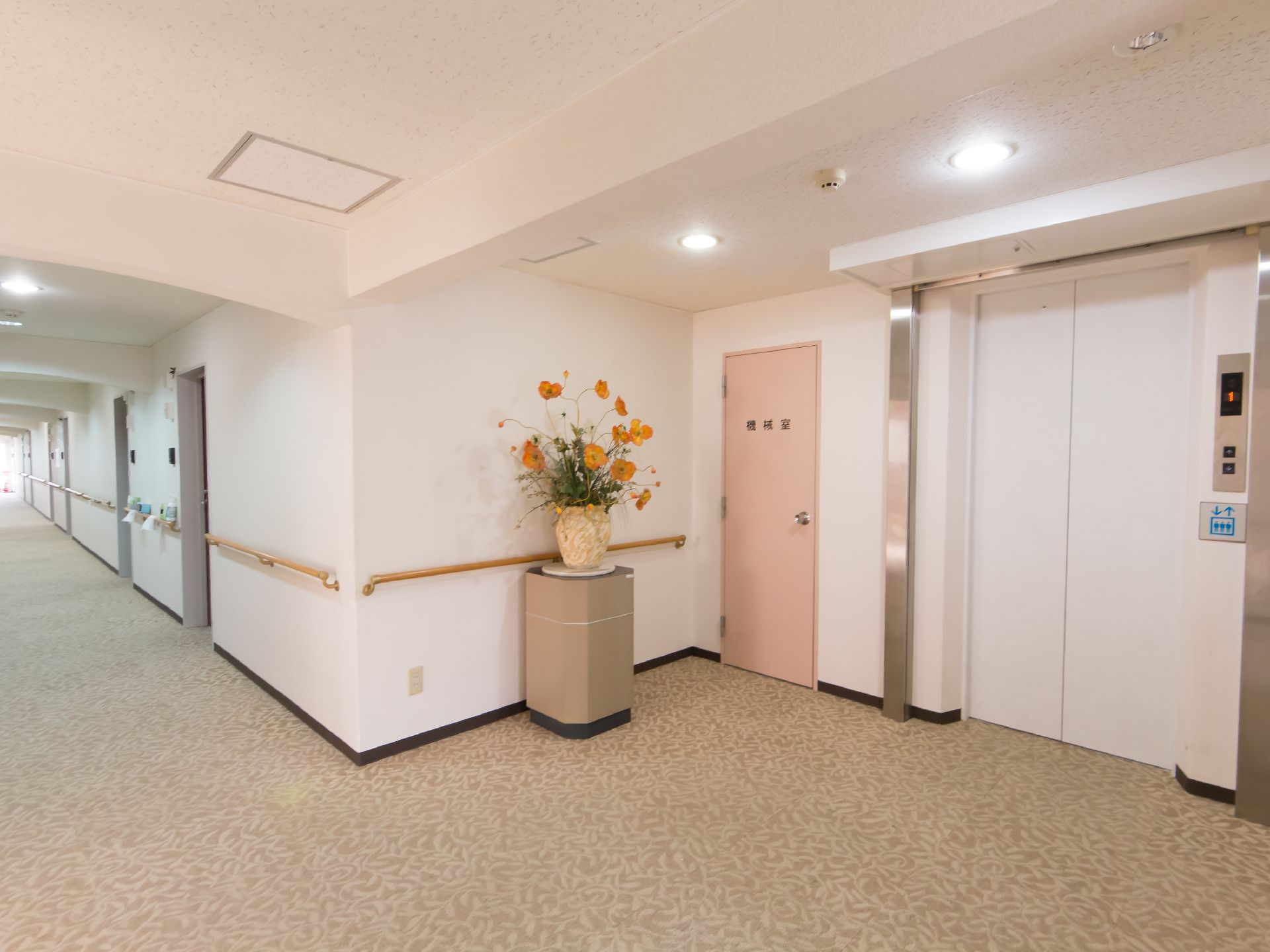 廊下は落ち着いたデザインの床面になっている。エレベーター乗降口の横には、花瓶に生けられた花が置かれている。