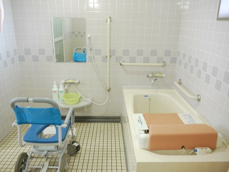 青い浴室用車いすがシャワーの前にあり、その横にはリフト付きの浴槽がある。