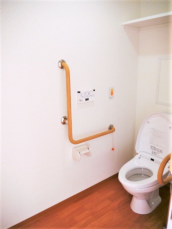両サイドに手すりが付いたトイレは温水洗浄便座で、すぐそばに呼び出しボタンも付いている。