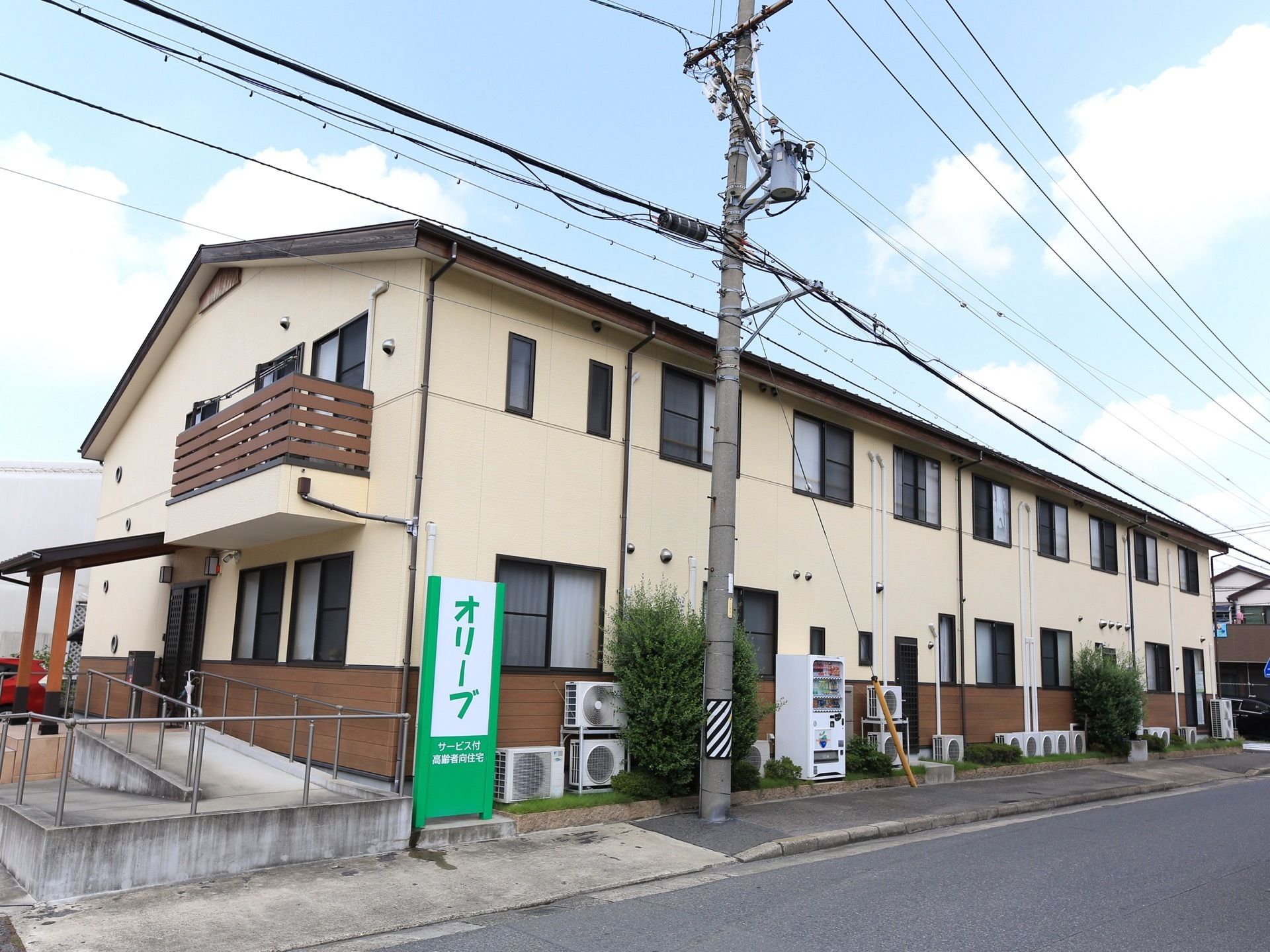 ベージュ系とブラウン系の２色でデザインされた２階建ての施設である。グリーン系の施設看板が印象的である。