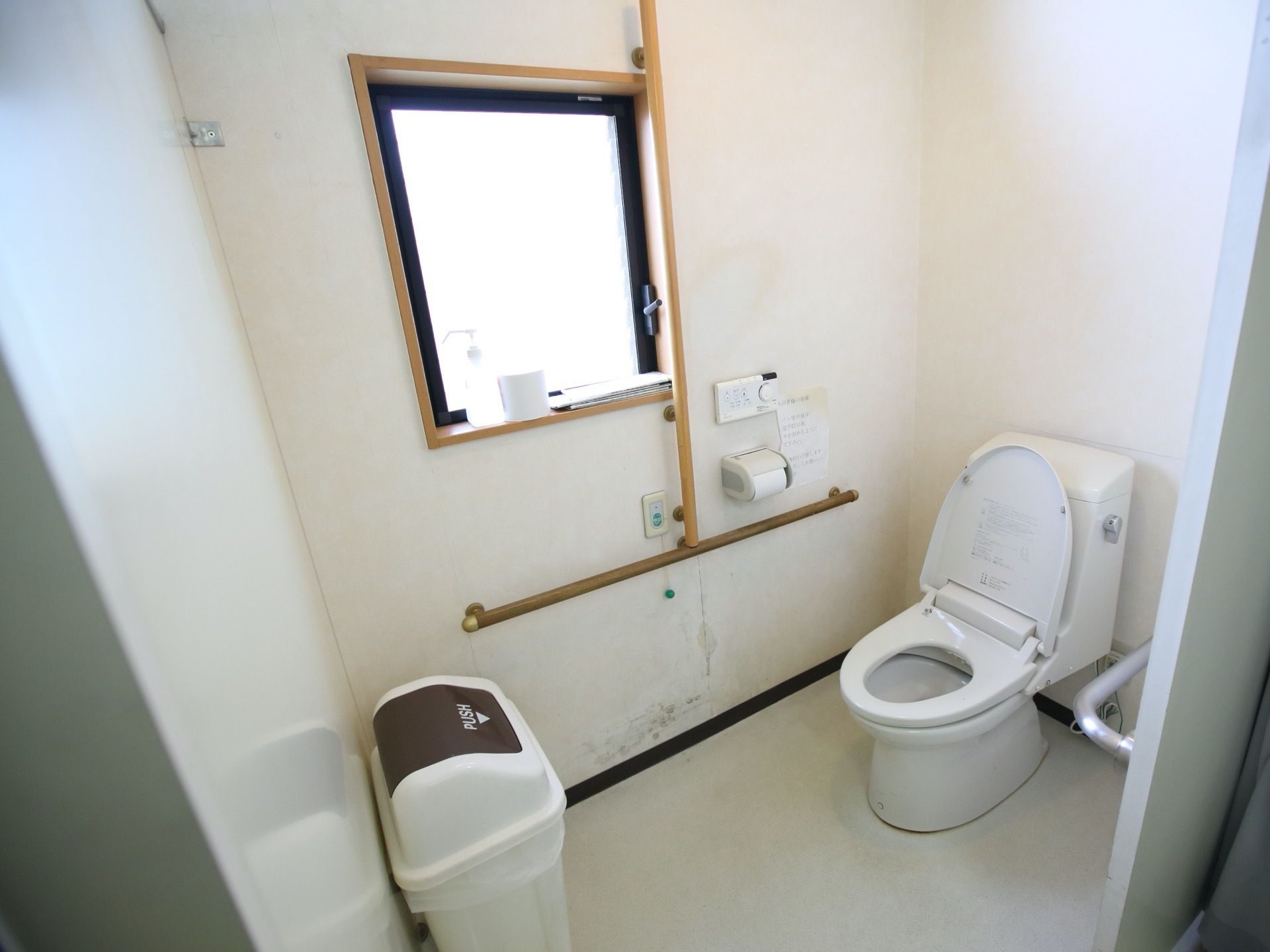 洋式便座を備えたトイレである。大きなゴミ箱が置かれている。壁側には縦横に手すりががある。
