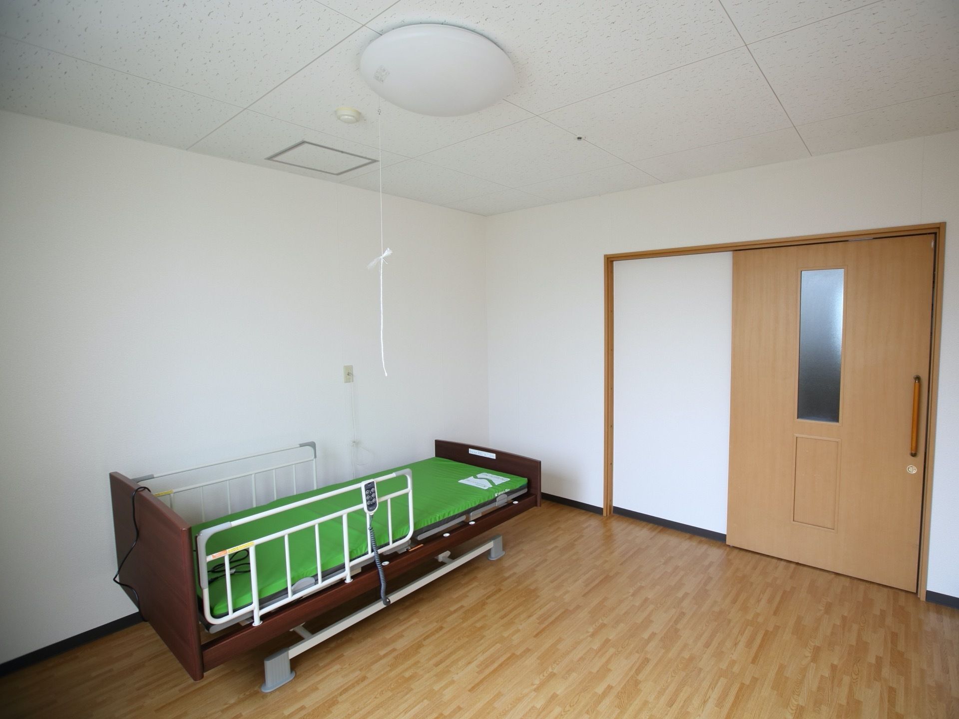丸型の照明を完備した、広い居室である。扉に縦長の明かり窓が設置されている。グリーンのマットが敷かれた、ベッドもある。