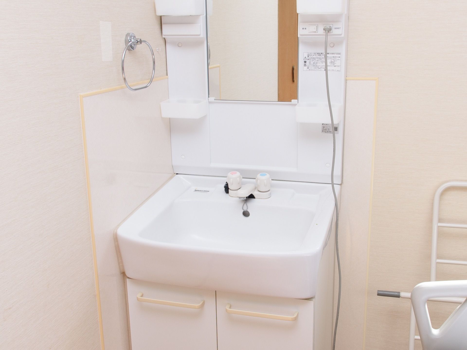 鏡付きの洗面台である。扉付き棚や小物を収納できるスペースがある。水撥ねしても水滴をふき取りやすい壁紙を取り付けている。