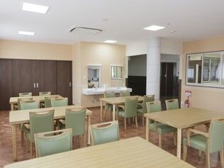 4人掛けのテーブルセットが並んだ食堂はフローリングで奥には車いす対応の洗面所がある。テーブルの上には何も置かれておらず、きれいに整理整頓されている。