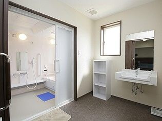 広い脱衣所が付いた浴室。浴室内の洗い場も広く、浴室のドアはワイドタイプ。脱衣所には洗面所や体重計、棚もあり、浴室内にはシャワーも付いている。