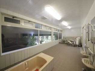機械浴が設置された広い浴室の壁の一面には窓が付いていて、外を眺めることができる。手前には浴槽があり、壁にはシャワーが付いている。