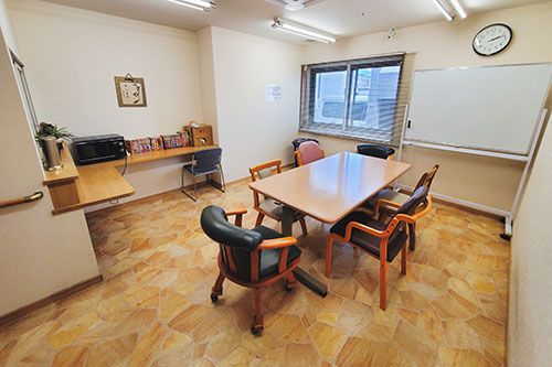テーブルを囲んで話しているピンクのポロシャツを着た女性スタッフと眼鏡をかけた高齢女性。