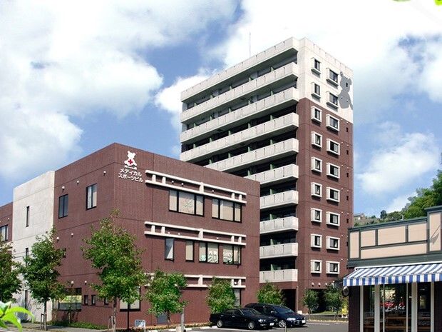ブラウン系の高さの異なる建物が２つあり、外壁には施設名が書かれている。敷地内には駐車場もある。