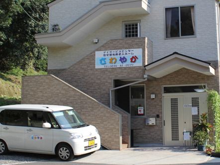 眼鏡をかけた高齢男性が福祉車両から降りようとしていて、そばにいる若いスタッフが手伝っている。