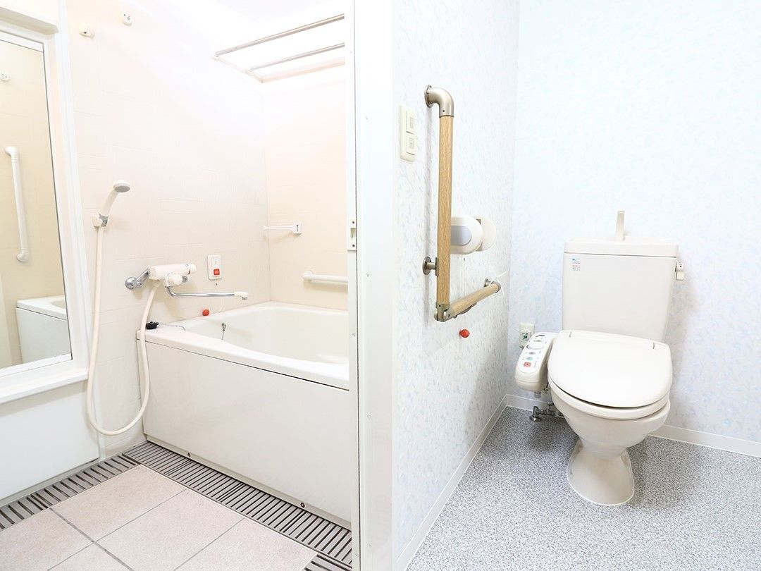 右手にトイレ、左手に浴室があり、それぞれ白を基調とし、手すりや呼び出しボタンがある。