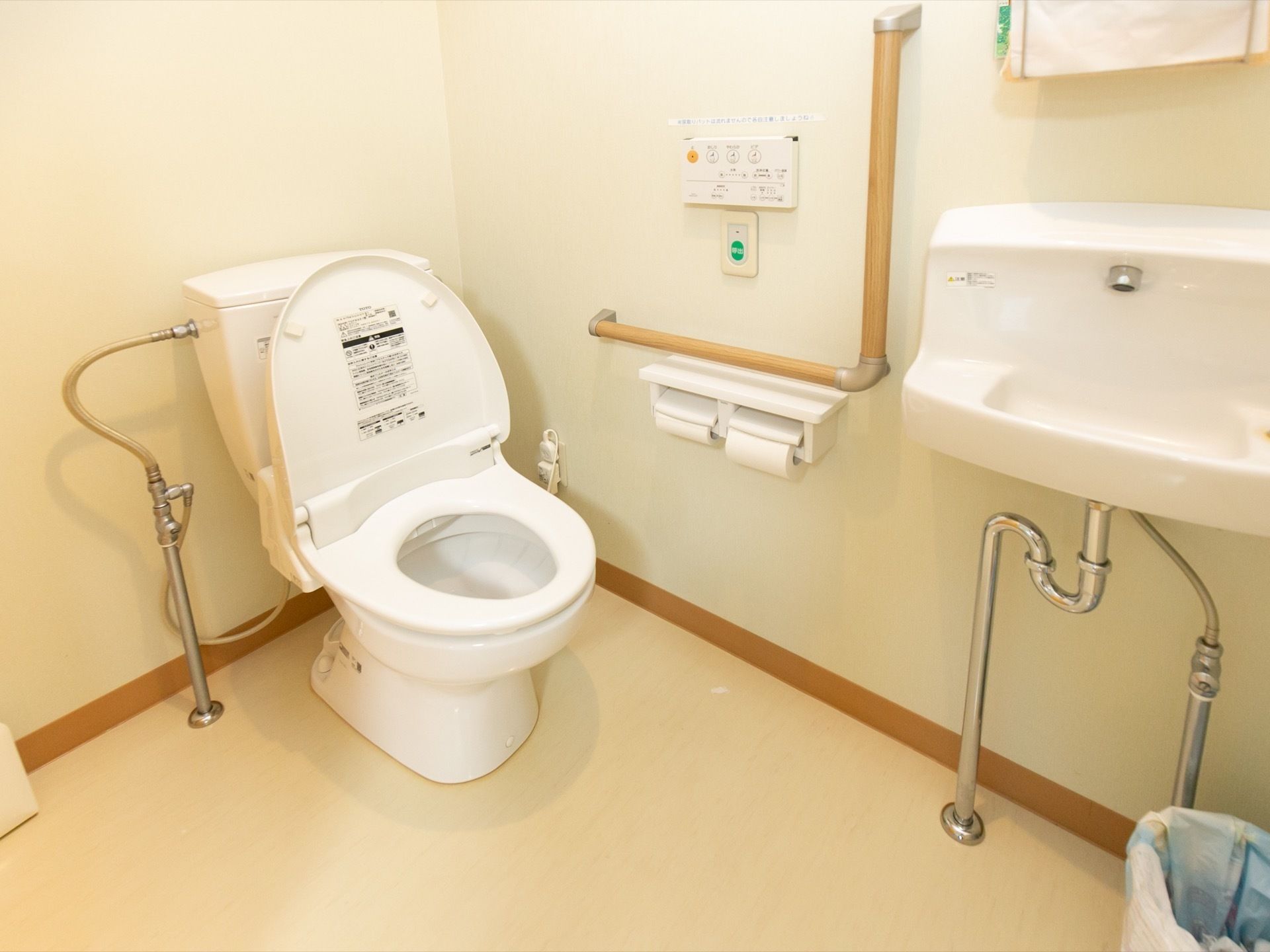 車椅子でも入れる充分な広さのトイレである。壁にはＬ字型の手すりや呼び出しボタン、トイレットペーパーホルダーなどが設置されている。