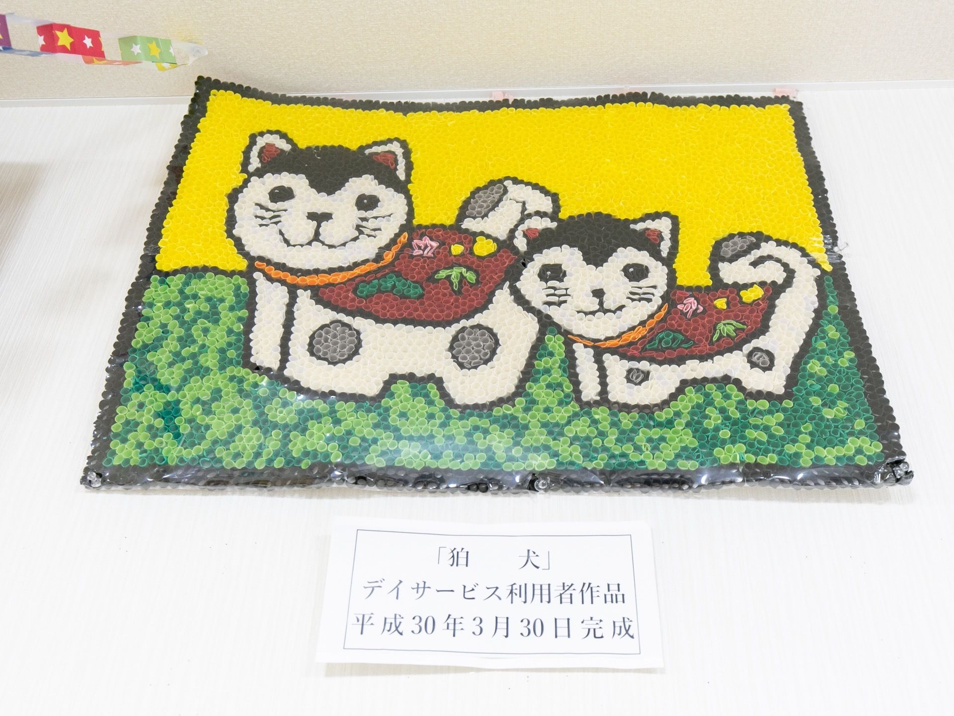 壁に入居者の作品が掲示されている。ビーズのようなもので描かれた狛犬の絵で、とてもかわいらしい作品である。