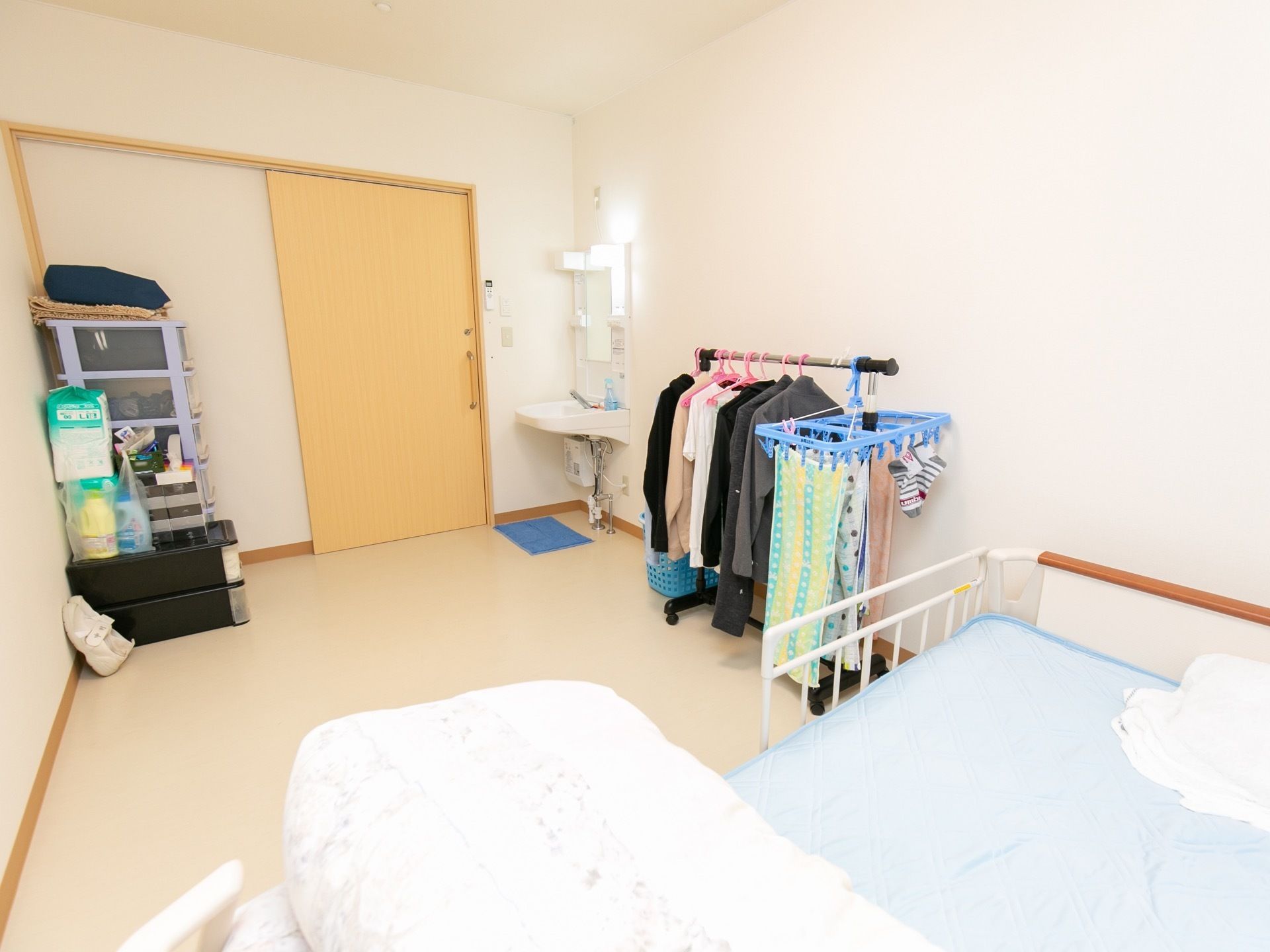 白を基調としたシンプルな造りの居室である。入口は木目調の引き戸になっており、近くには洗面台が設置されている。