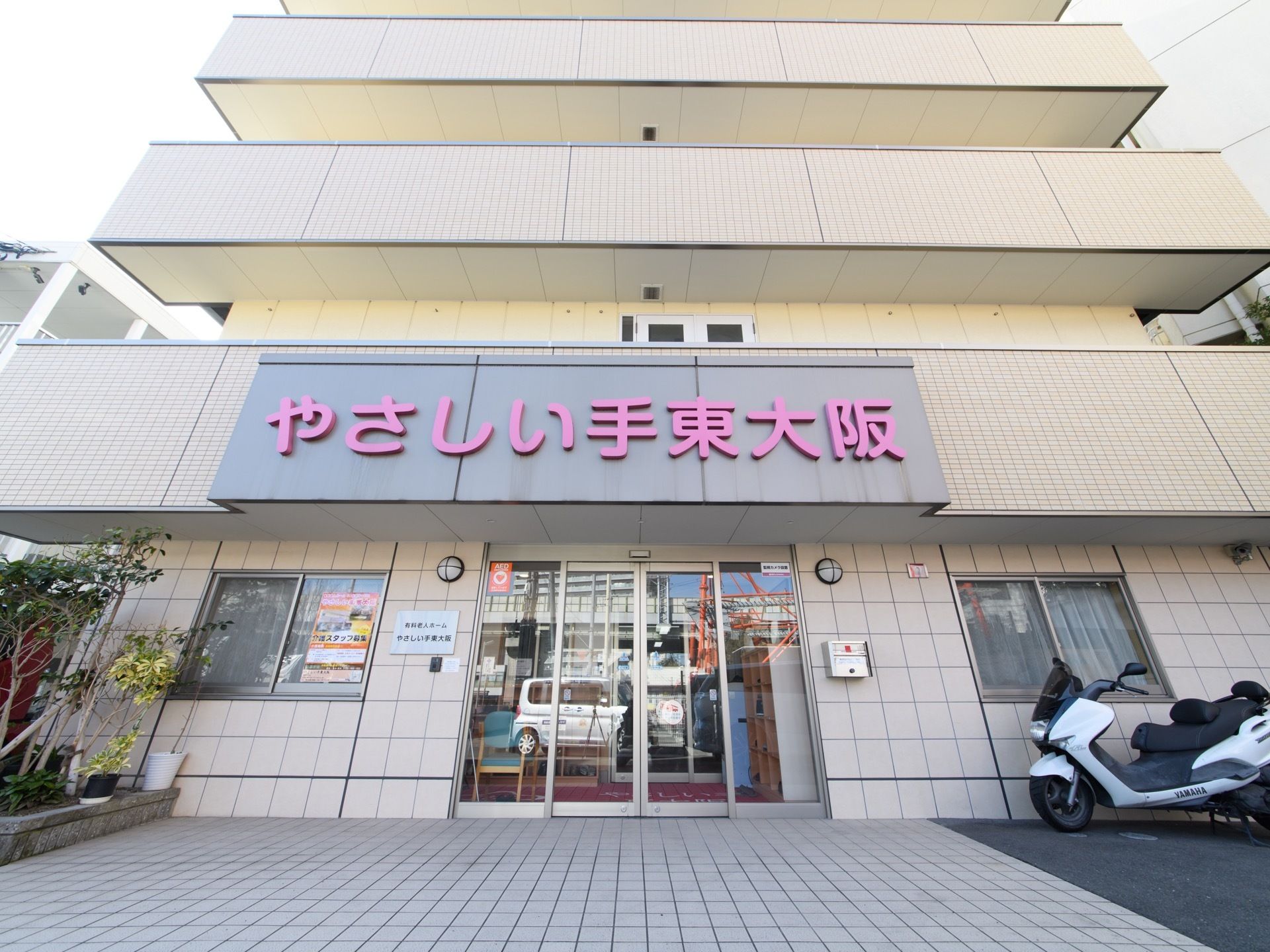 アイボリー色の優しい外観にピンクの施設名が大きく玄関前に飾られてとても目立っている。玄関前はバリアフリー対応になっている。