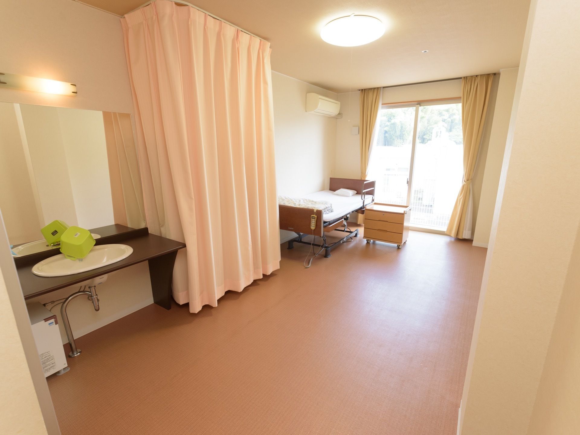 車椅子対応型の洗面台を備えた居室には、カーテンで仕切られたトイレを設置している。大きな掃き出し窓のため、大変明るく開放的な空間である。