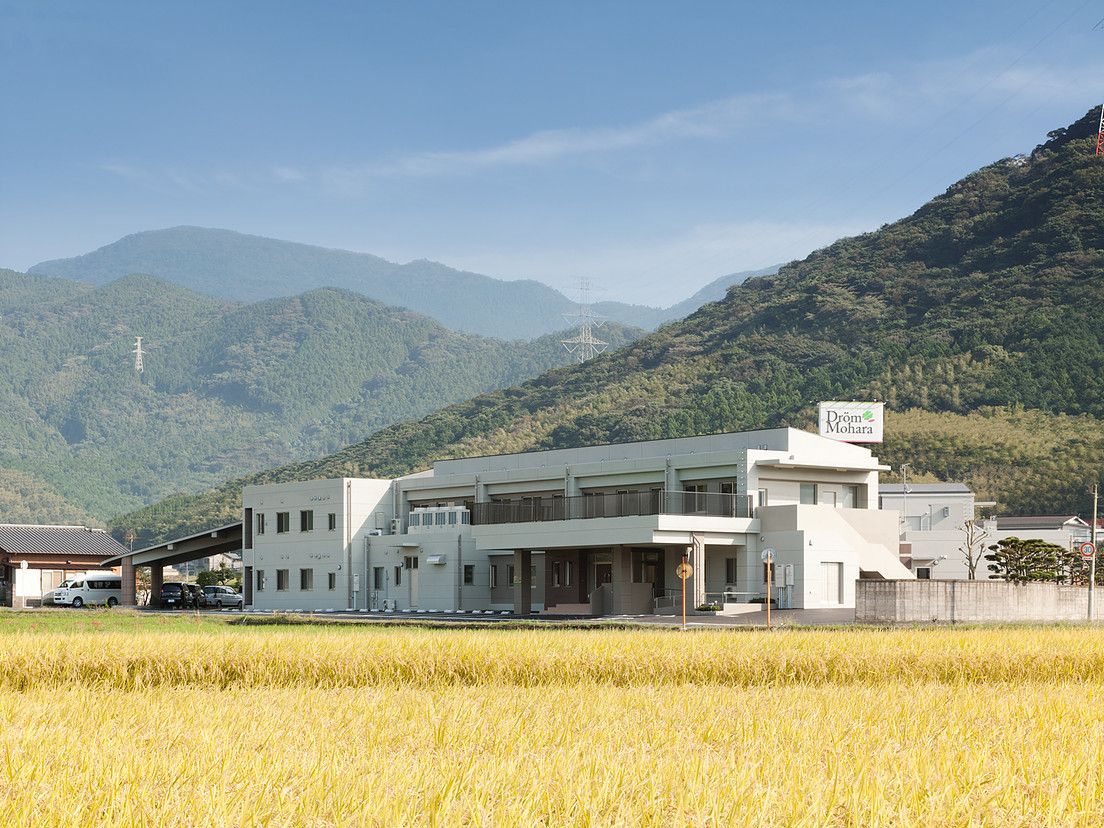 山と田んぼに囲まれた施設を写した写真。鉄骨造の清潔感ある建物が写っている