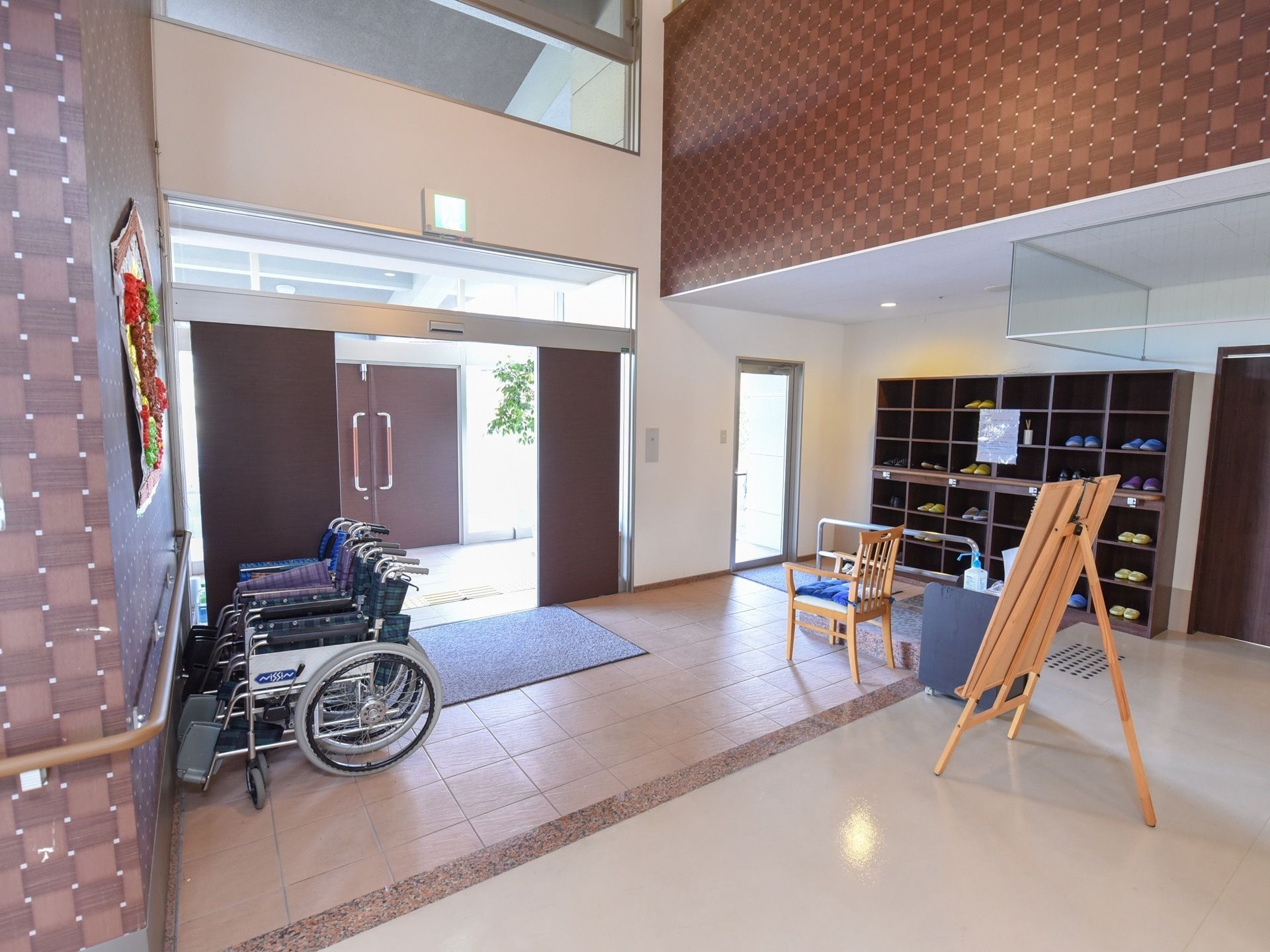 天井が吹き抜けになっている開放的なエントランス。壁沿いには靴箱や、複数の車椅子が畳んで用意されている。
