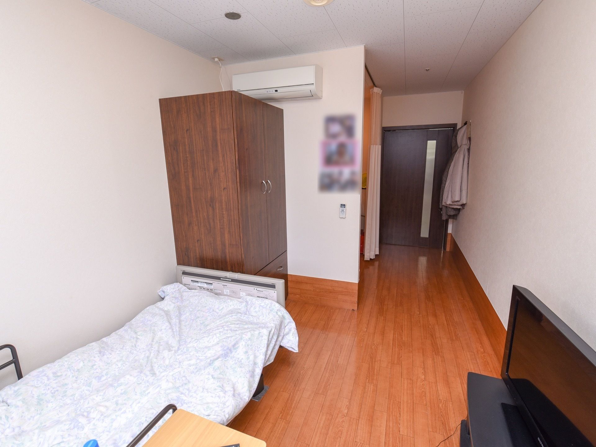 居室の入口は、縦に長いすりガラスが入った引き戸になっている。ベッドやエアコン、収納タンスが設置されている。