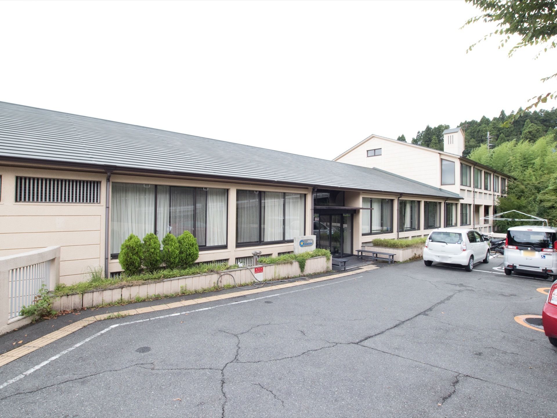 ２階建ての建物が見える。施設前方には生垣があり、さまざまな植物が植えらえている。入口まで点字ブロックが続いている。