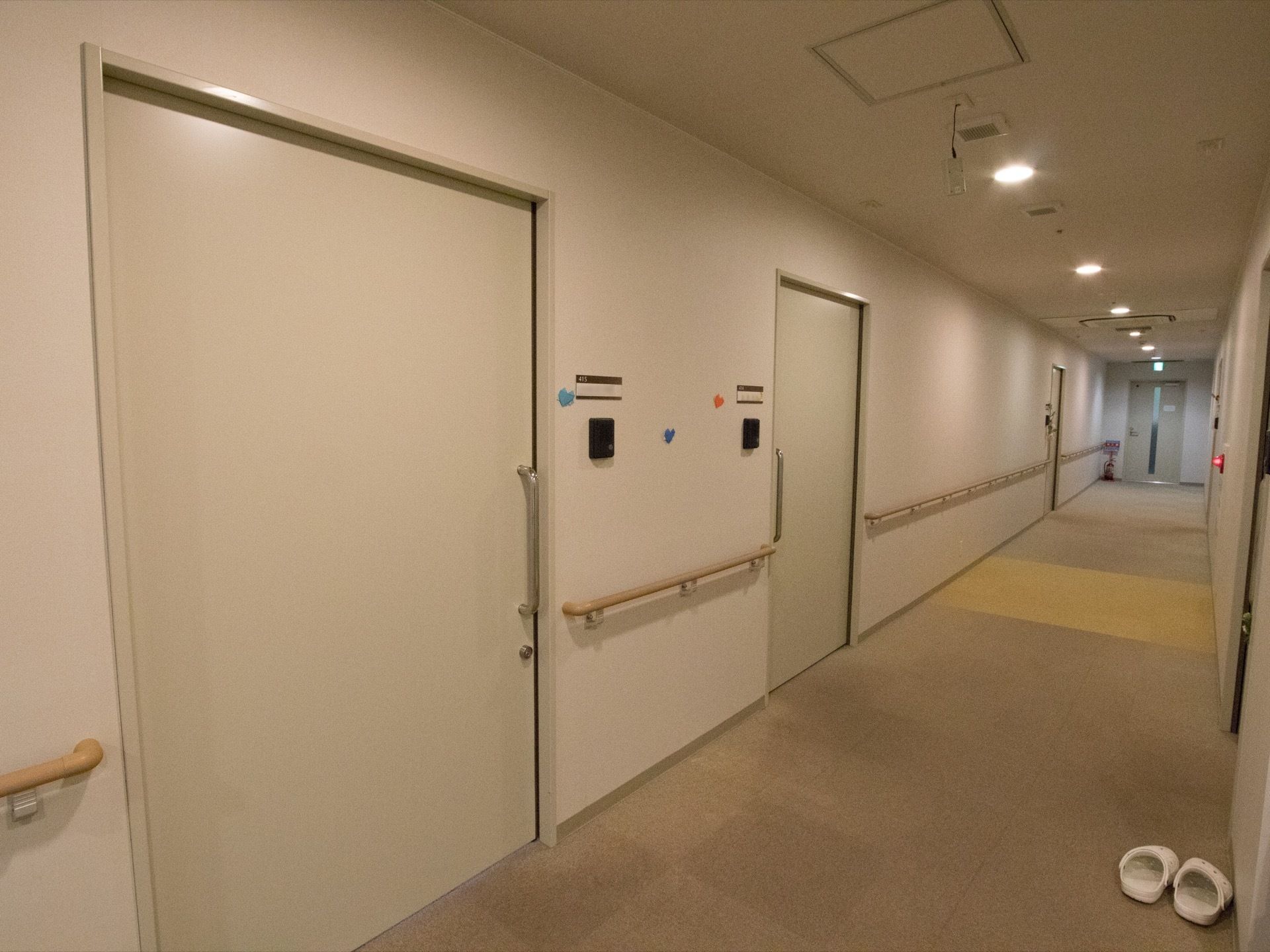 居室の扉の横にはインターホンが設置されている。壁には手すりが設けられている。非常ベルと消火器が見える。