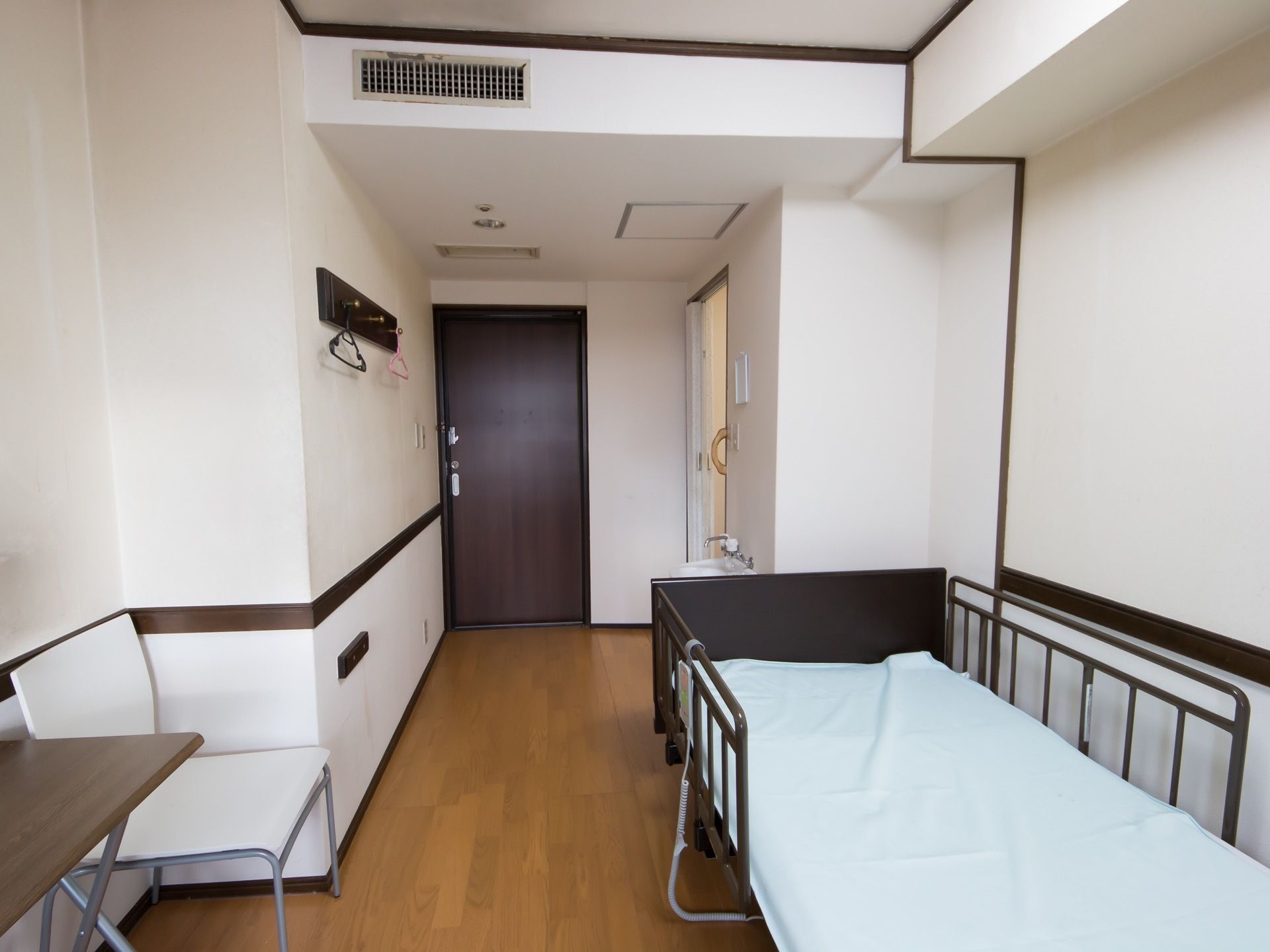 居室は、白色と茶色を基調とした落ち着いた空間になっている。転落防止柵つきのベッドやテーブル、椅子が設置されている。