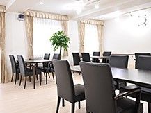 椅子とテーブルが並んでいる施設内の一室。食堂や喫茶室のような雰囲気の場所